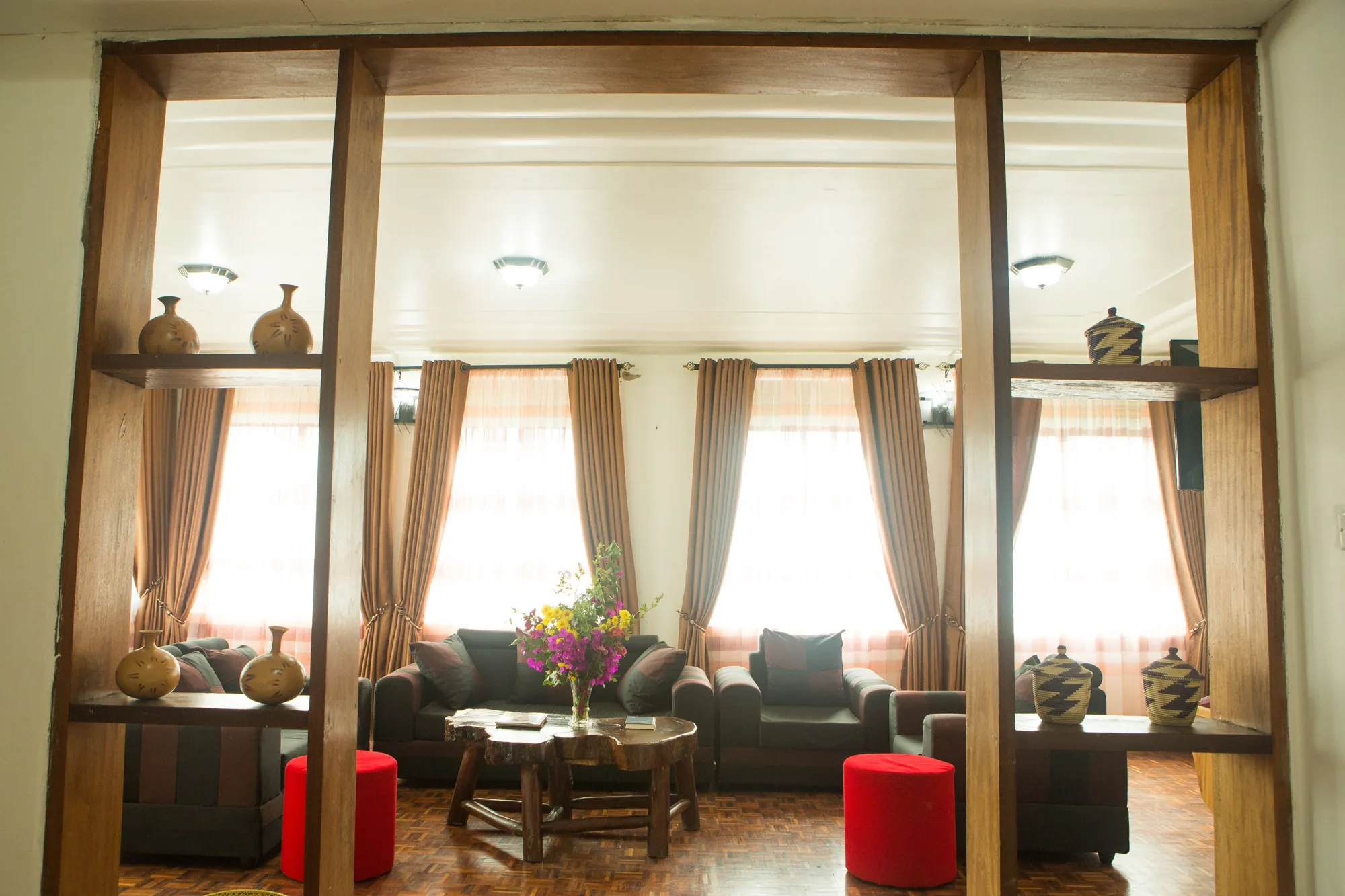 Family Suite: suite lounge with dark sofas, red stools and timber columns between the windows