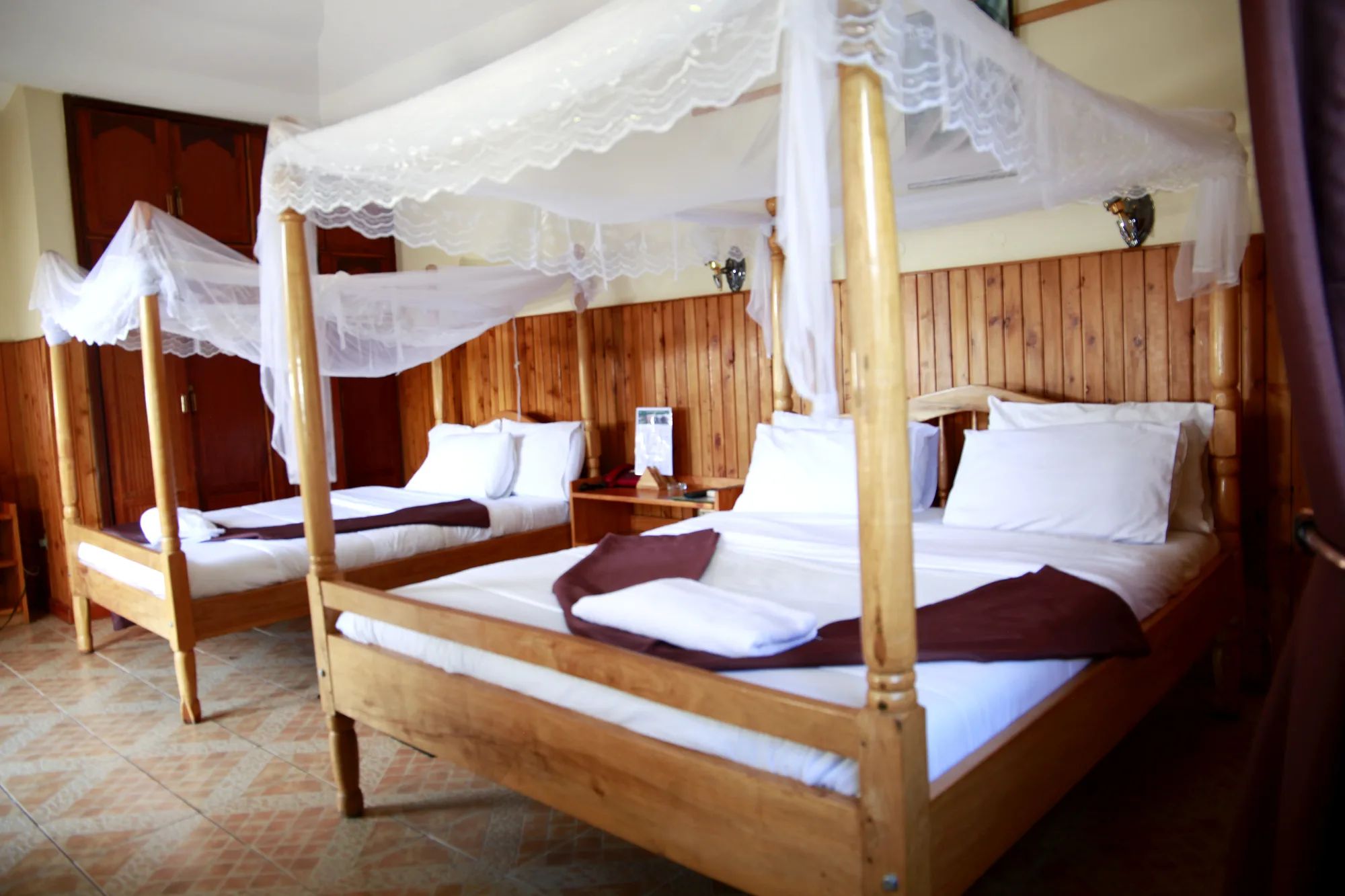 Family Suite: guest room with two beds under four-poster mosquito-net frames, timber-panelled walls, white linen and folded towels