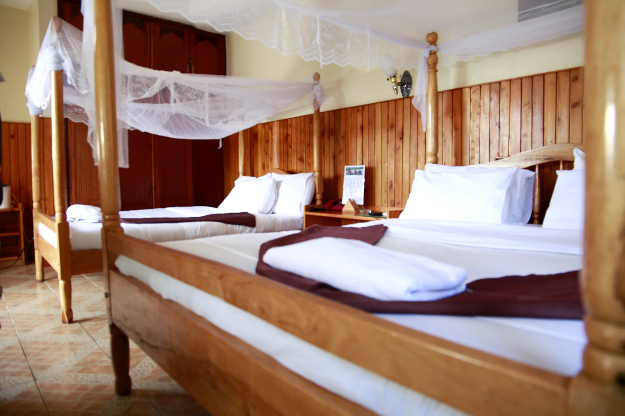 Family Suite: two beds with four-poster mosquito-net frames in a timber-panelled guest room with white linen and folded towels