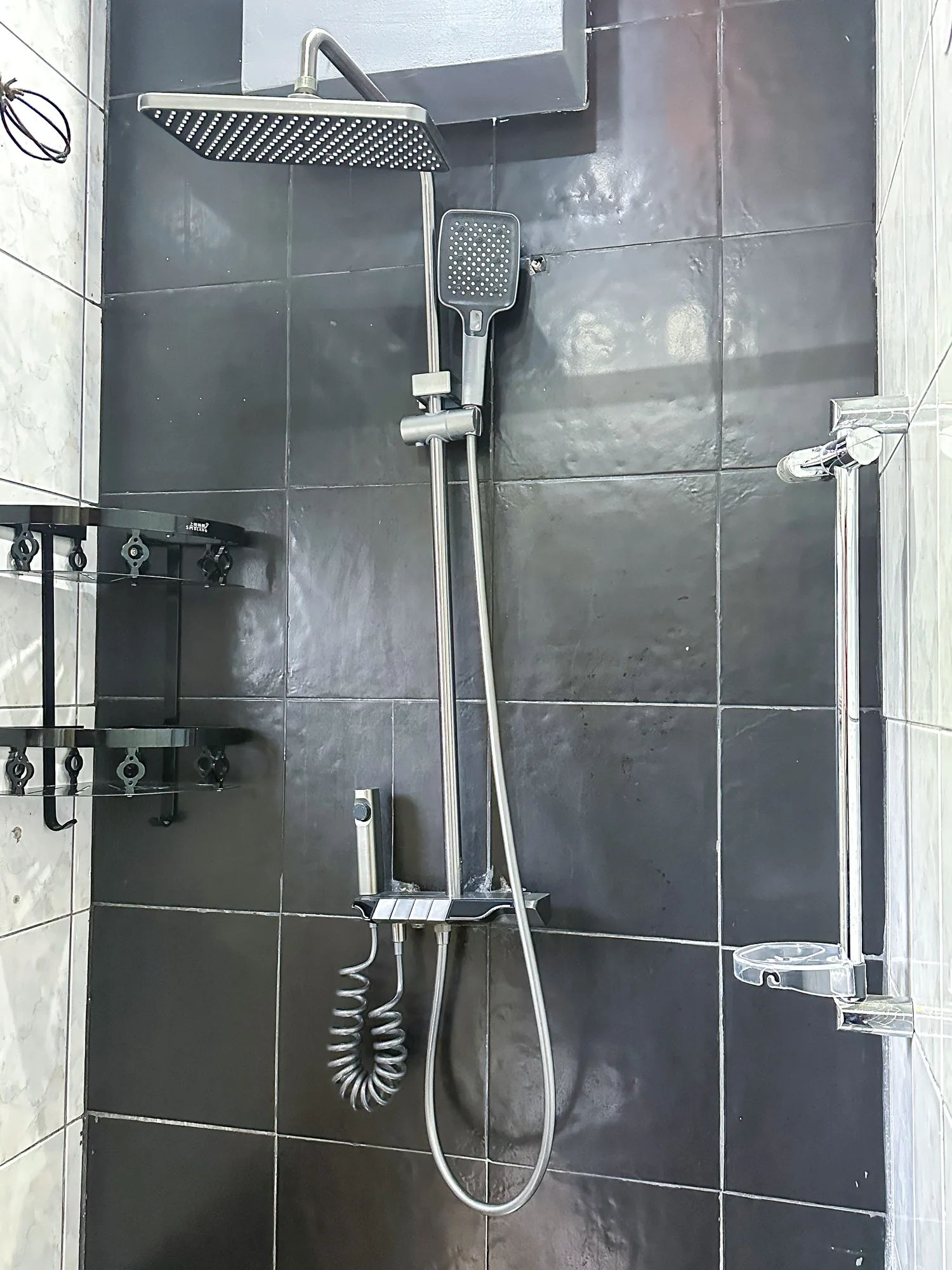 A dark-tiled shower cubicle with a rain head and hand shower