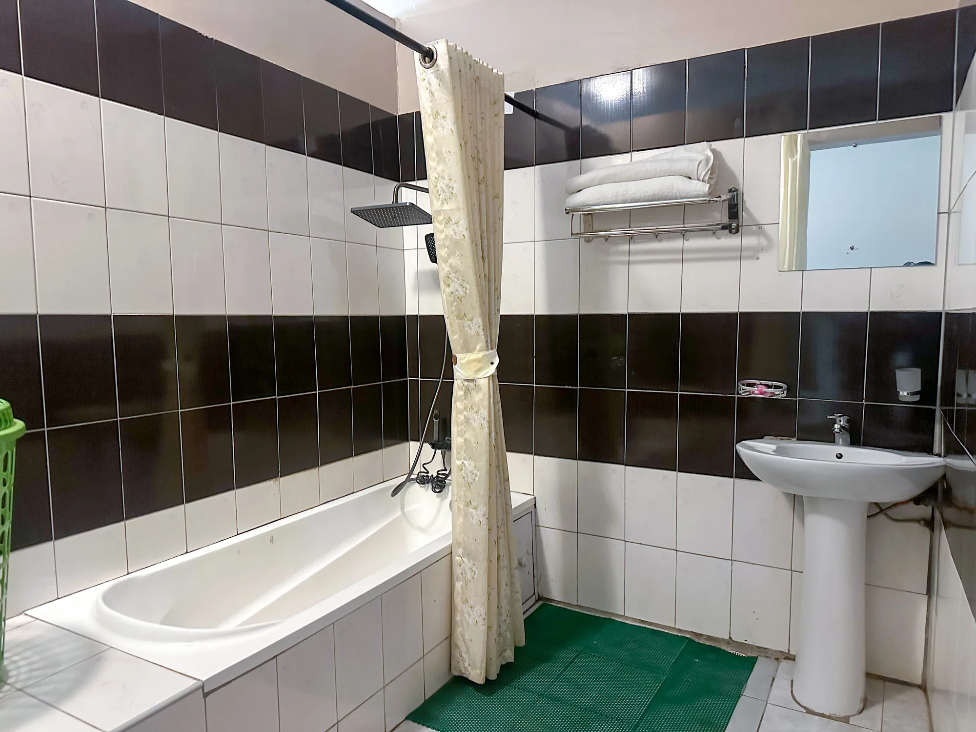 A bathroom with a bath under a shower curtain, basin and dark tiling