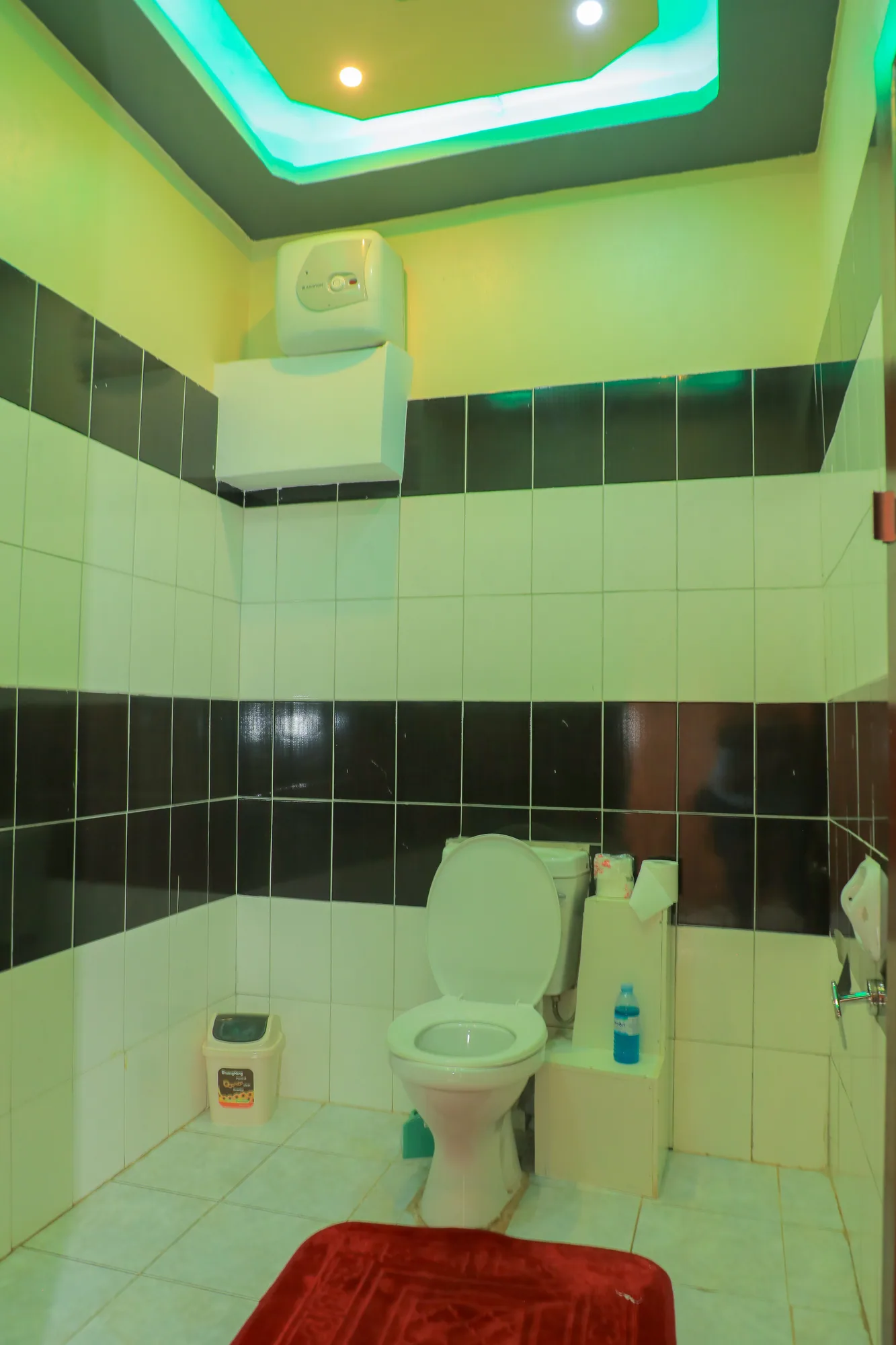 A green-tiled bathroom with a toilet and cistern under coloured ceiling lighting
