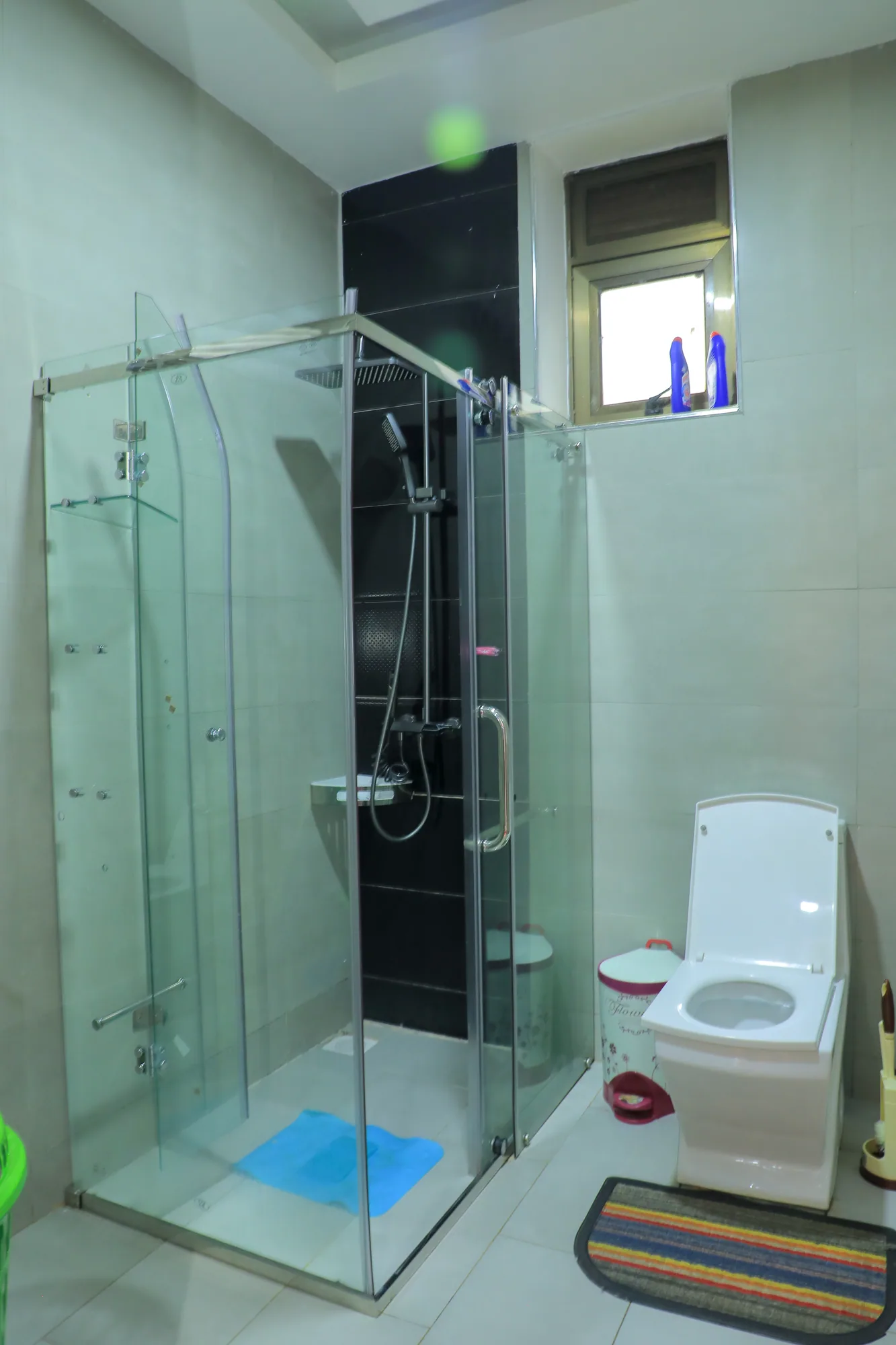 A glass shower enclosure beside the toilet in a white-tiled bathroom