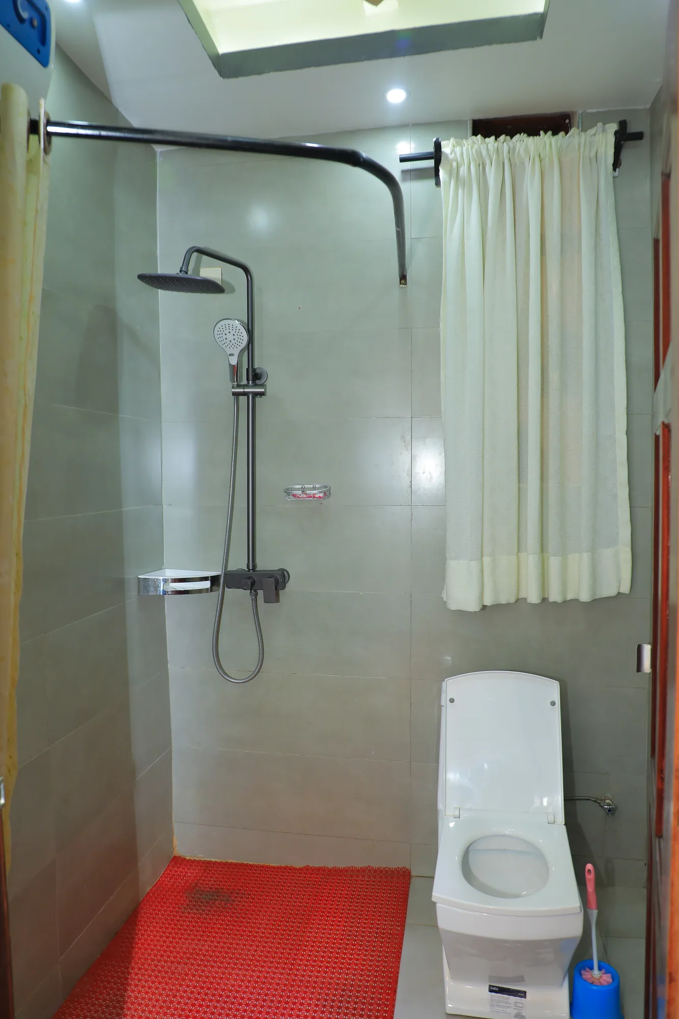 A shower with a curtain rail and toilet on a red bath mat
