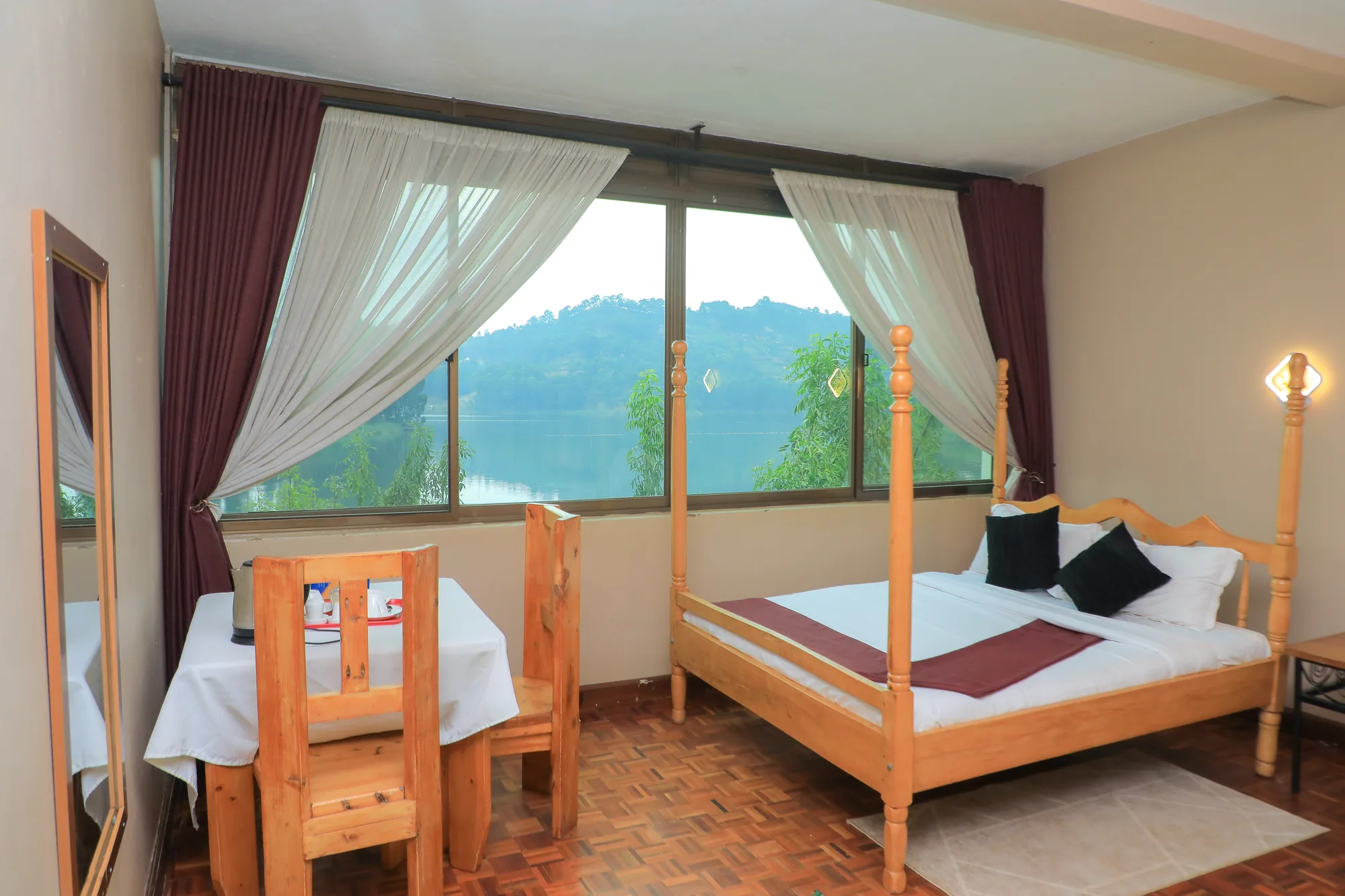A twin room with two beds and a small table beside a window with curtains open to the lake