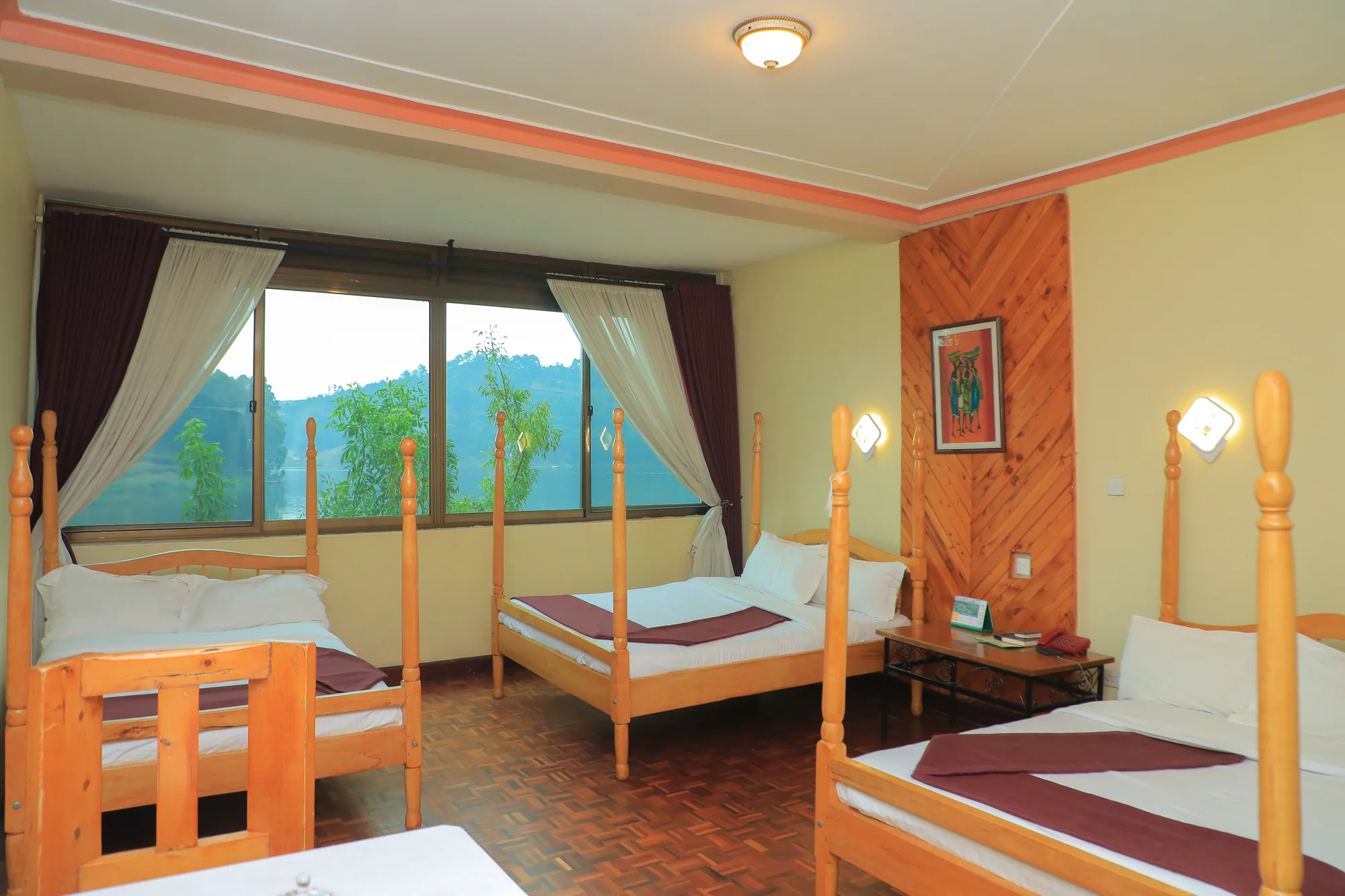 A triple room with three timber beds and a table under a curtained lake-facing window