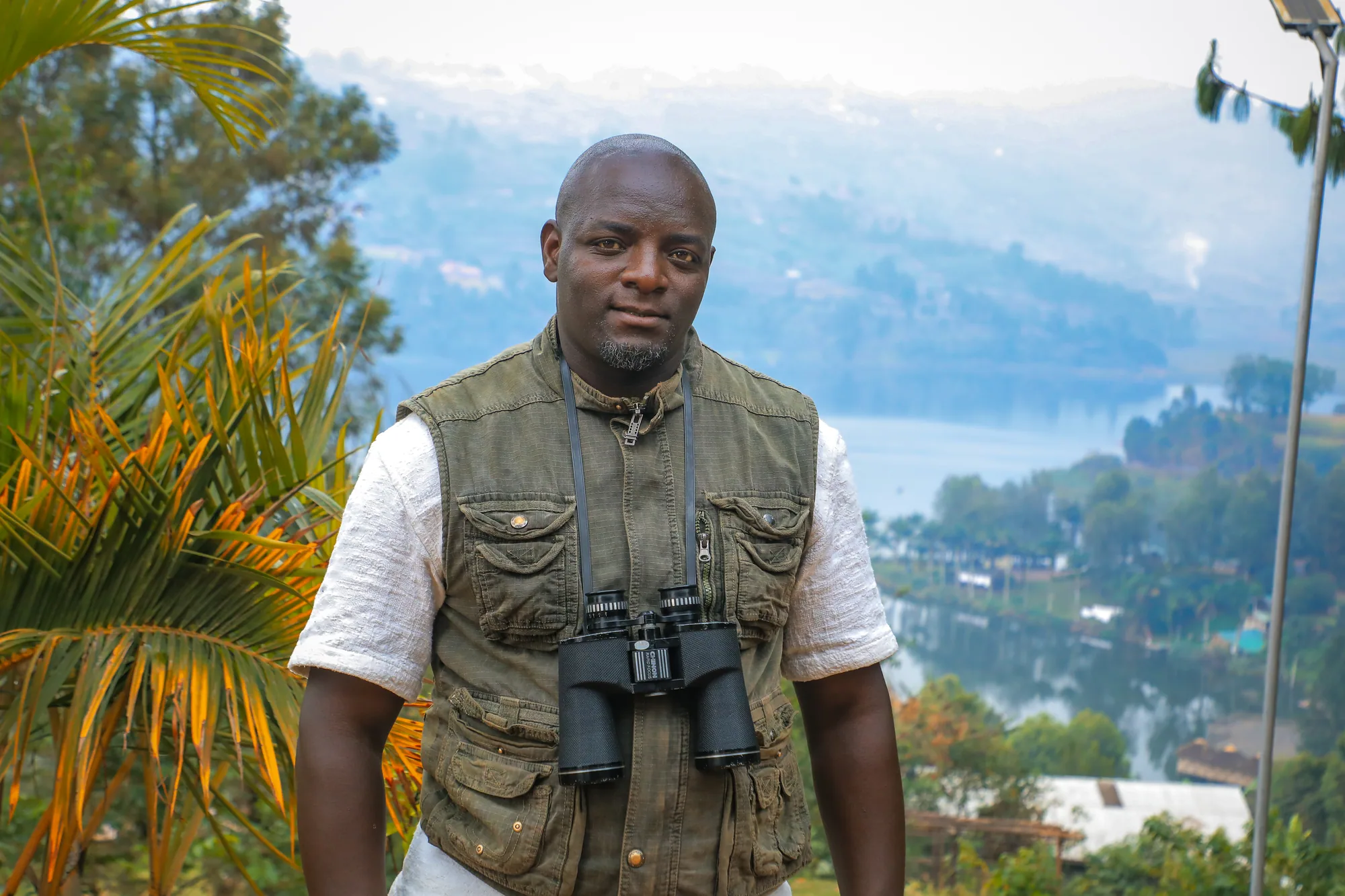A man with binoculars round his neck standing above the lake, looking to camera