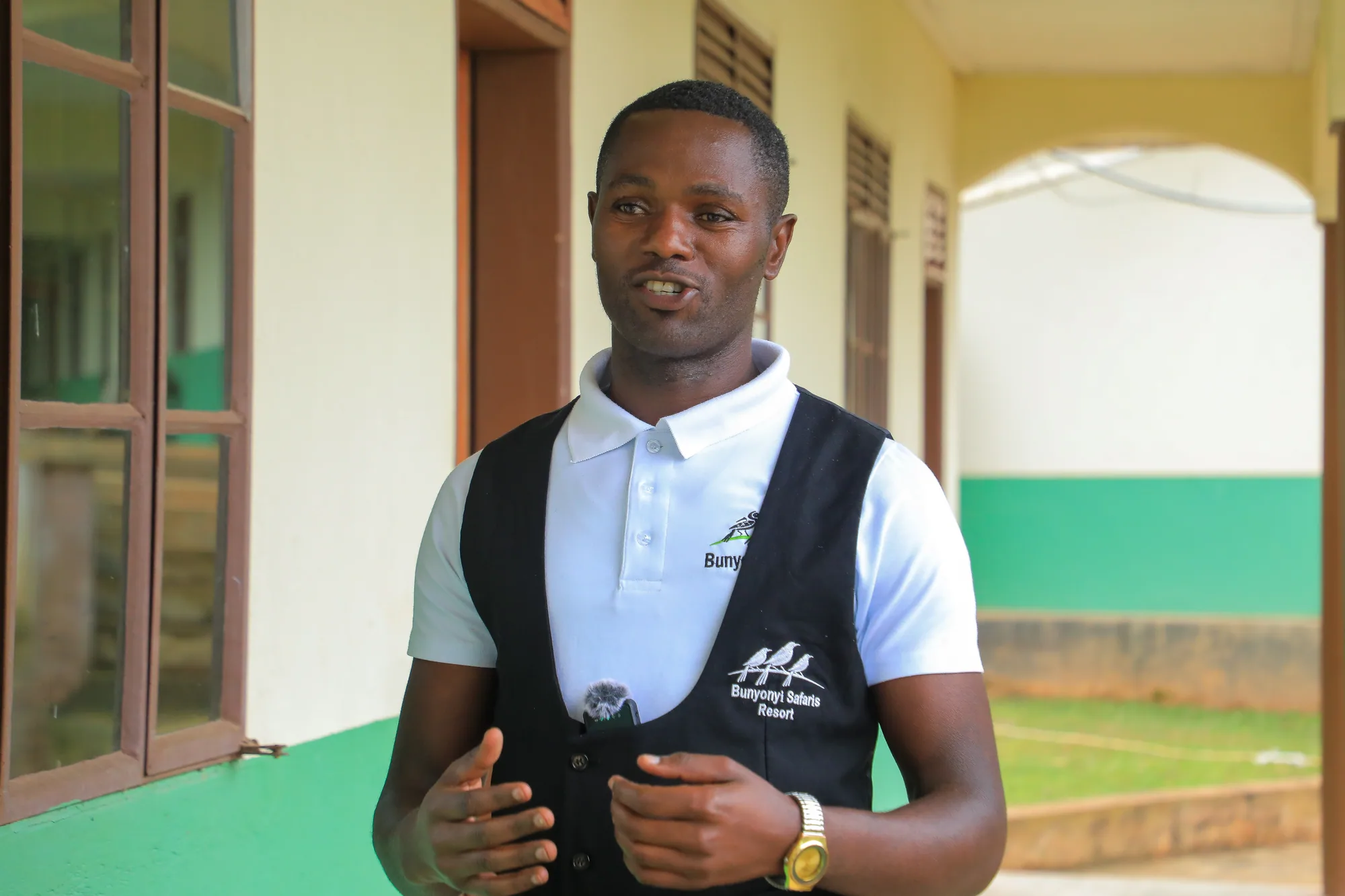 A staff member in a branded shirt and waistcoat speaking on the institute veranda