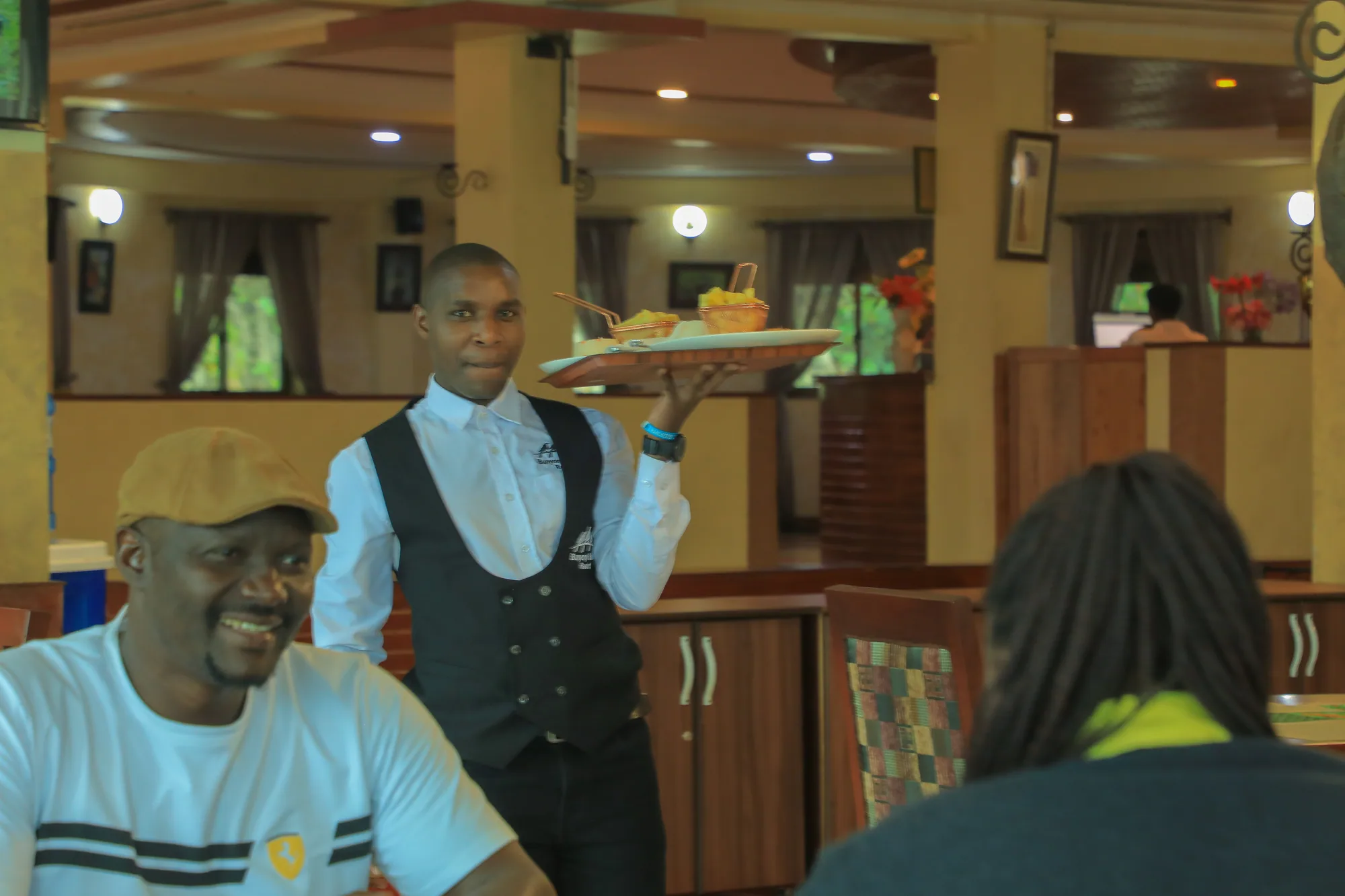 A waiter carrying a tray past a seated guest in the restaurant