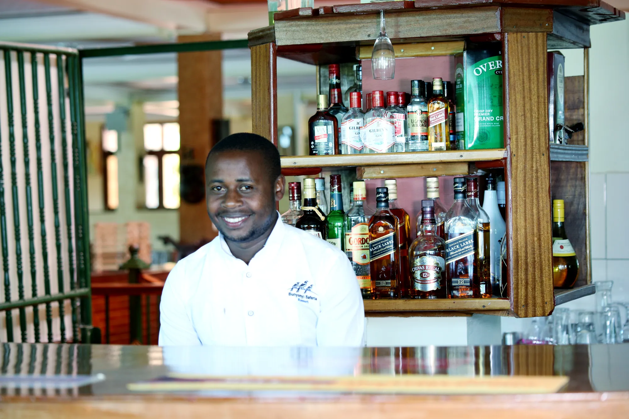 A barman in a branded shirt standing behind the spirits shelf at the bar