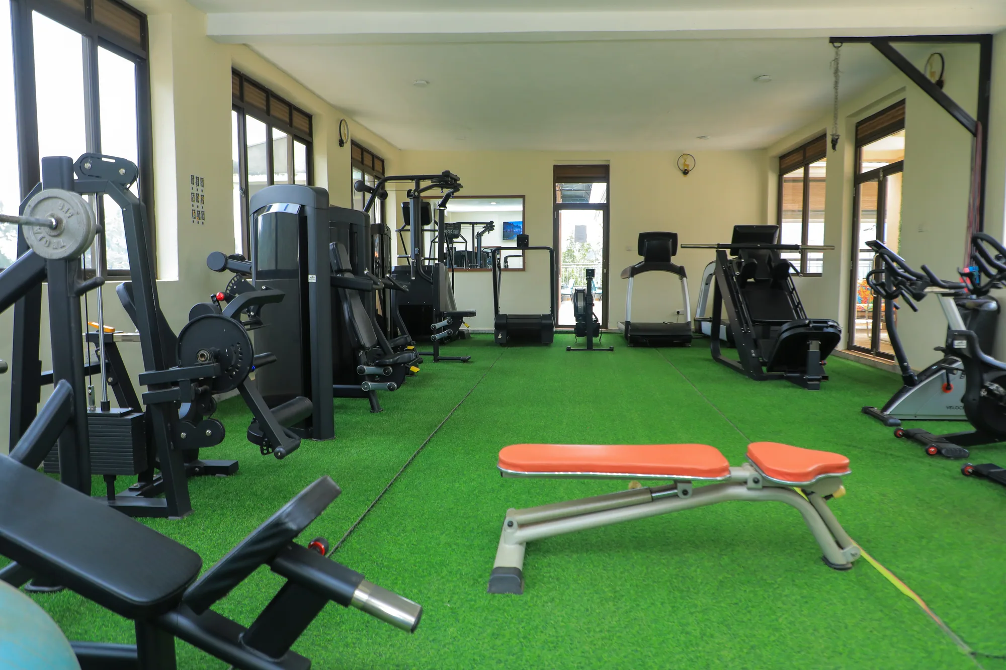 The gym's full length with weight stations, an orange bench and a treadmill