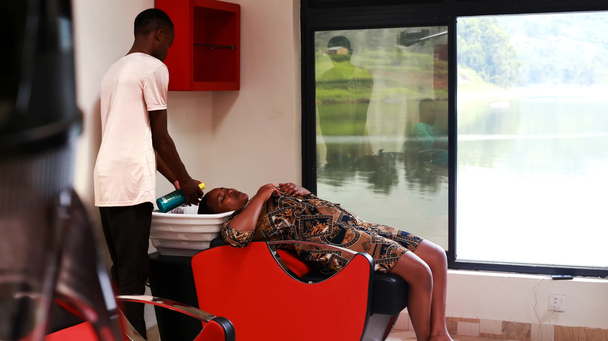 A stylist working on a client reclined in the salon chair by the window