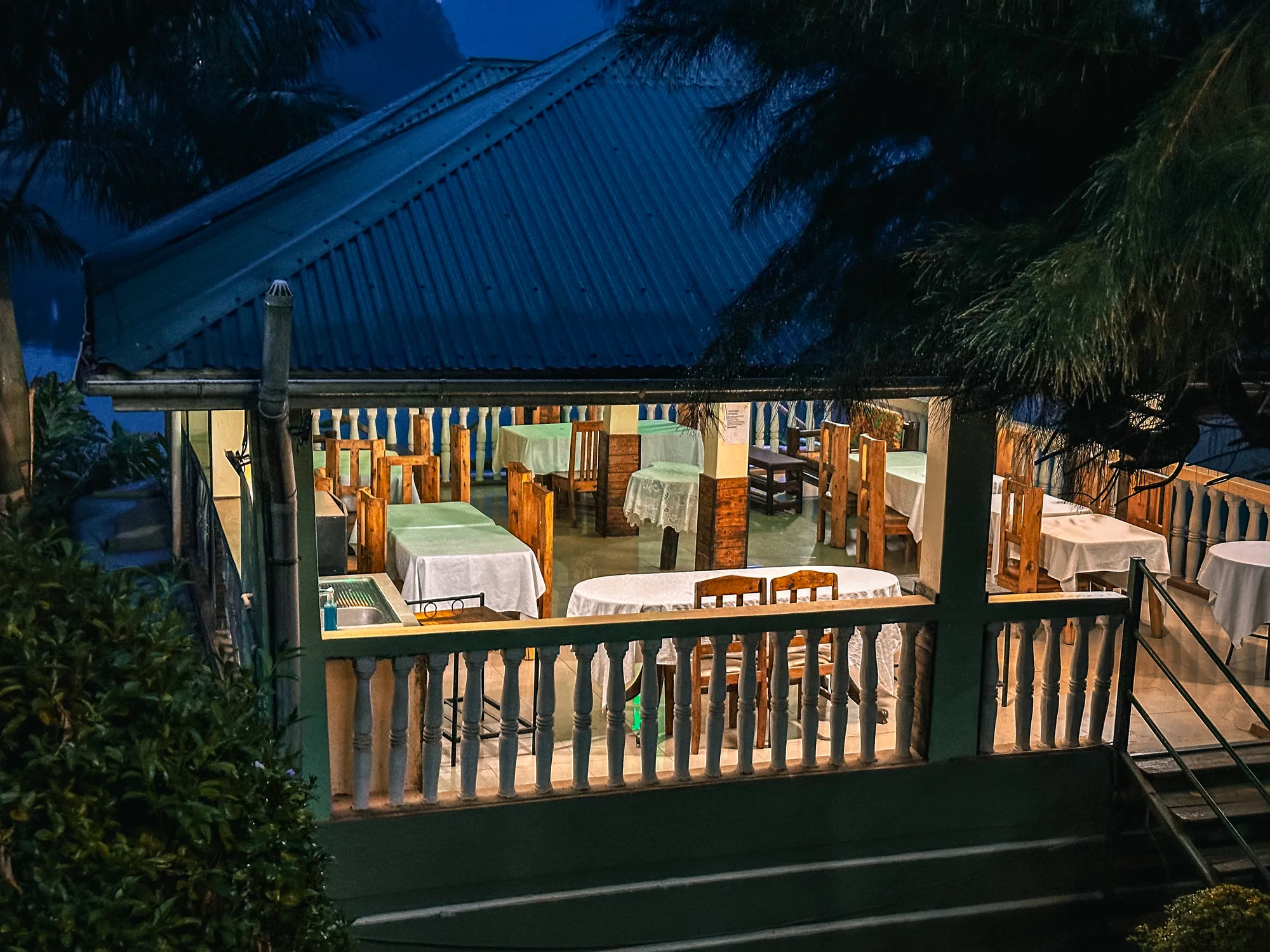A timber-railed veranda with tables lit at night