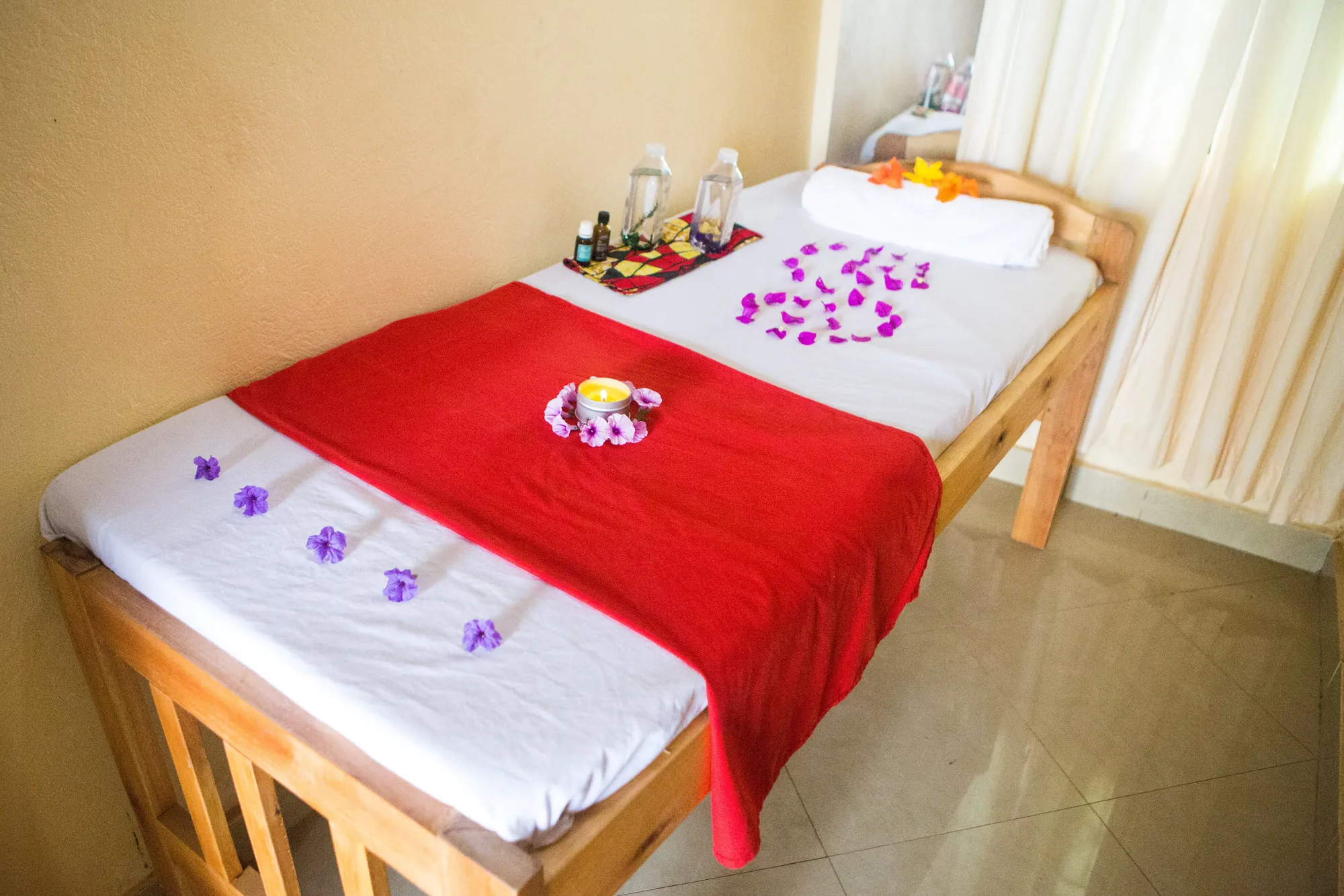 A massage couch made up with a red throw and petals, oils on the shelf behind