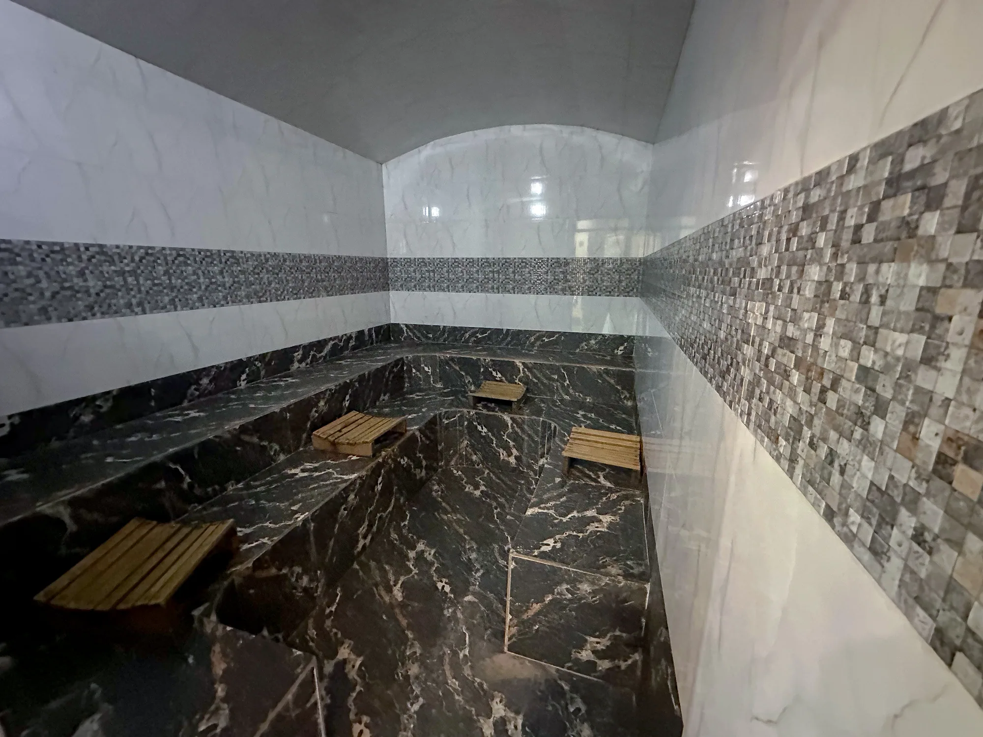 The steam room from the doorway, its dark marble walls and mosaic band